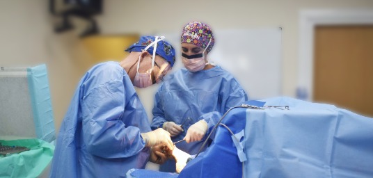 Our surgeon in scrubs with nurse performing foot surgery
